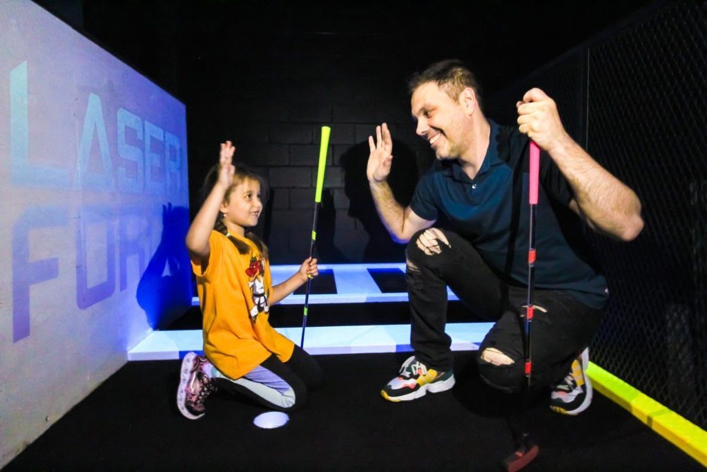 Enfant et parent qui jouent au mini-golf fluo
